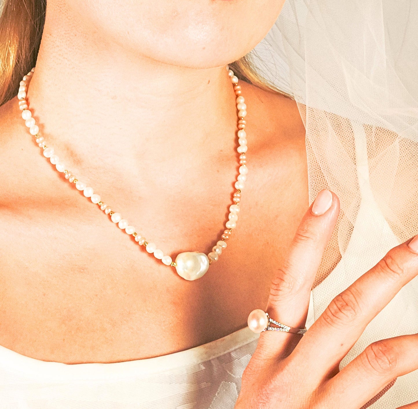 Pearl necklace and ring worn by a person, with a soft focus on the background.