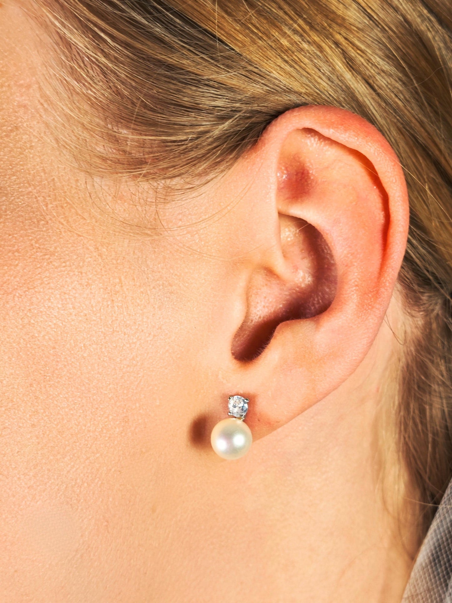 Close-up of an ear wearing a pearl earring with a clear gemstone.