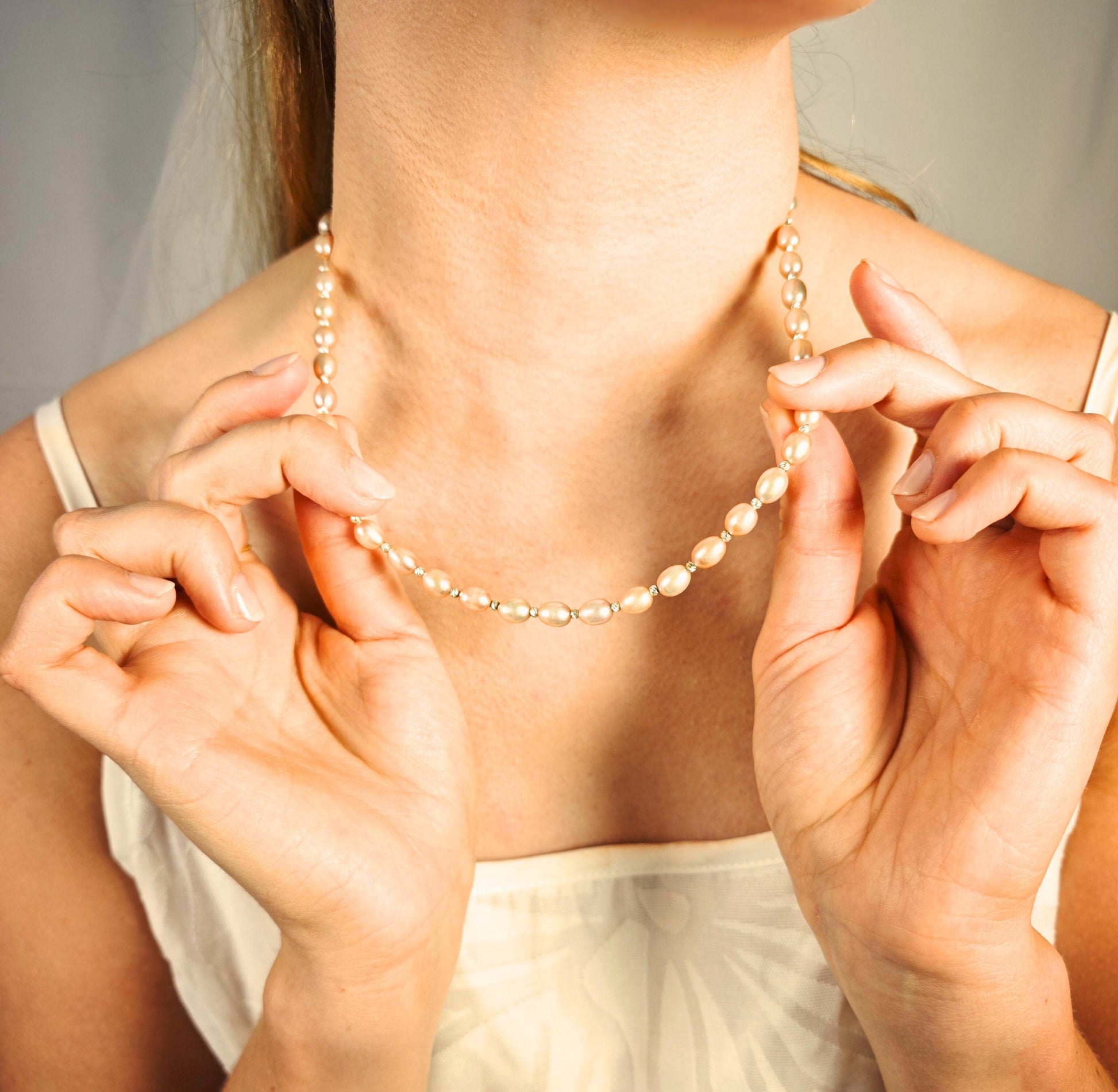 Person wearing a pearl necklace with hands adjusting it