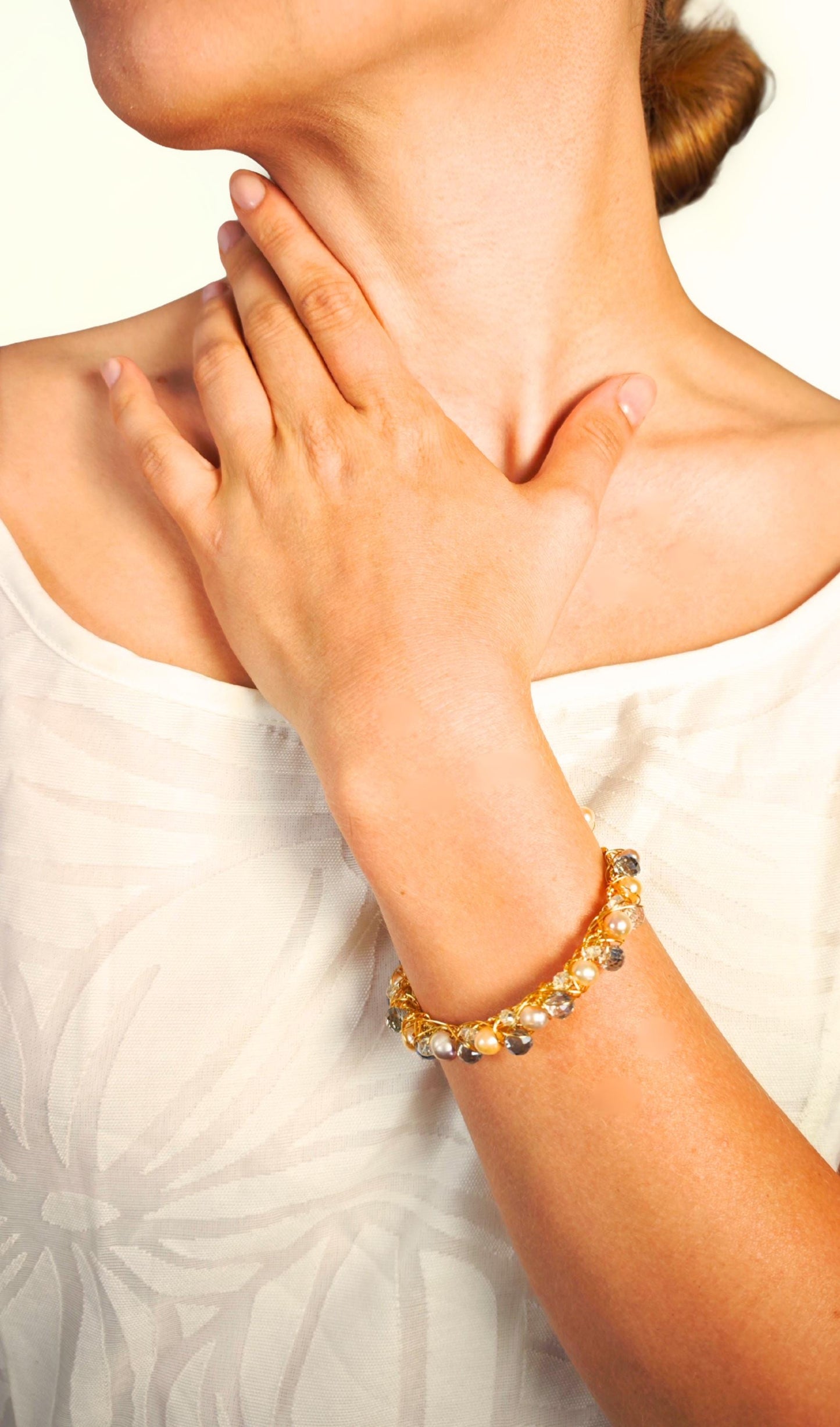 Close-up of a person wearing a gold bracelet on a neutral background