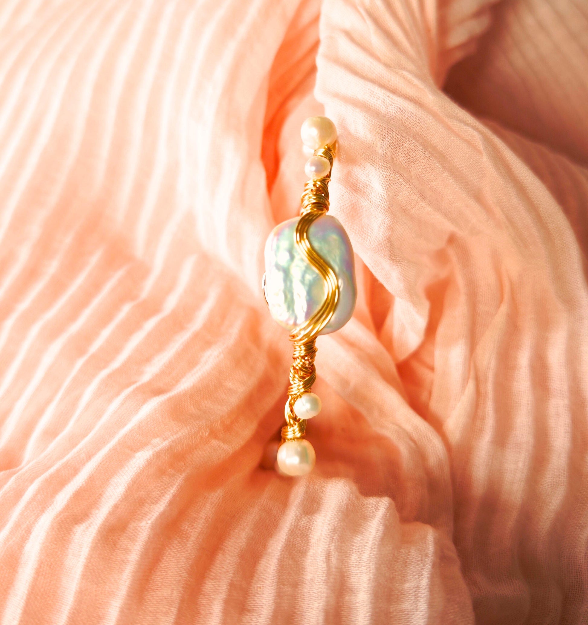 Gold and pearl earring on a pink fabric background