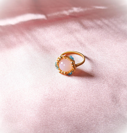 Gold ring with a pink gemstone on a soft pink fabric background