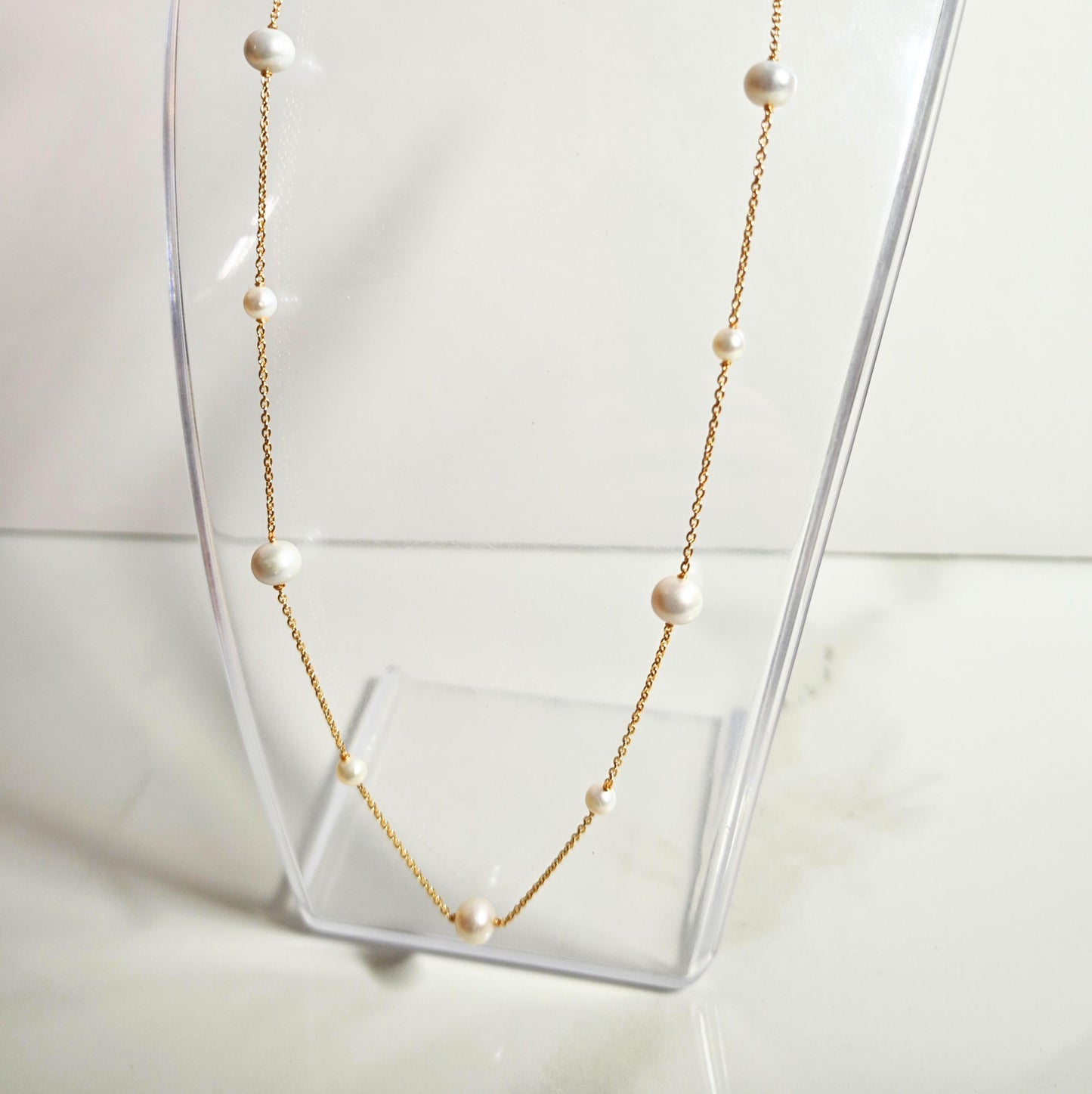 Pearl necklace on a clear stand with a white background