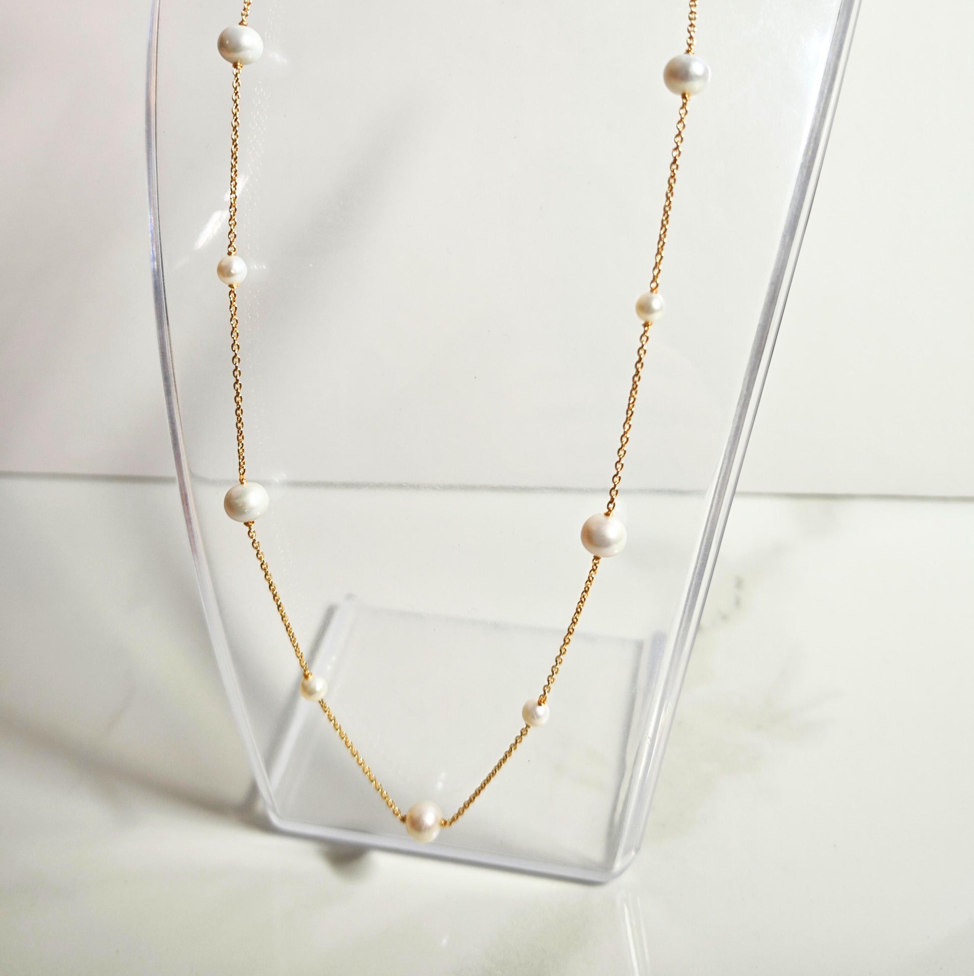 Pearl necklace on a clear stand with a white background