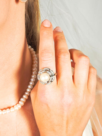 Close-up of a hand wearing a pearl ring with a blurred background