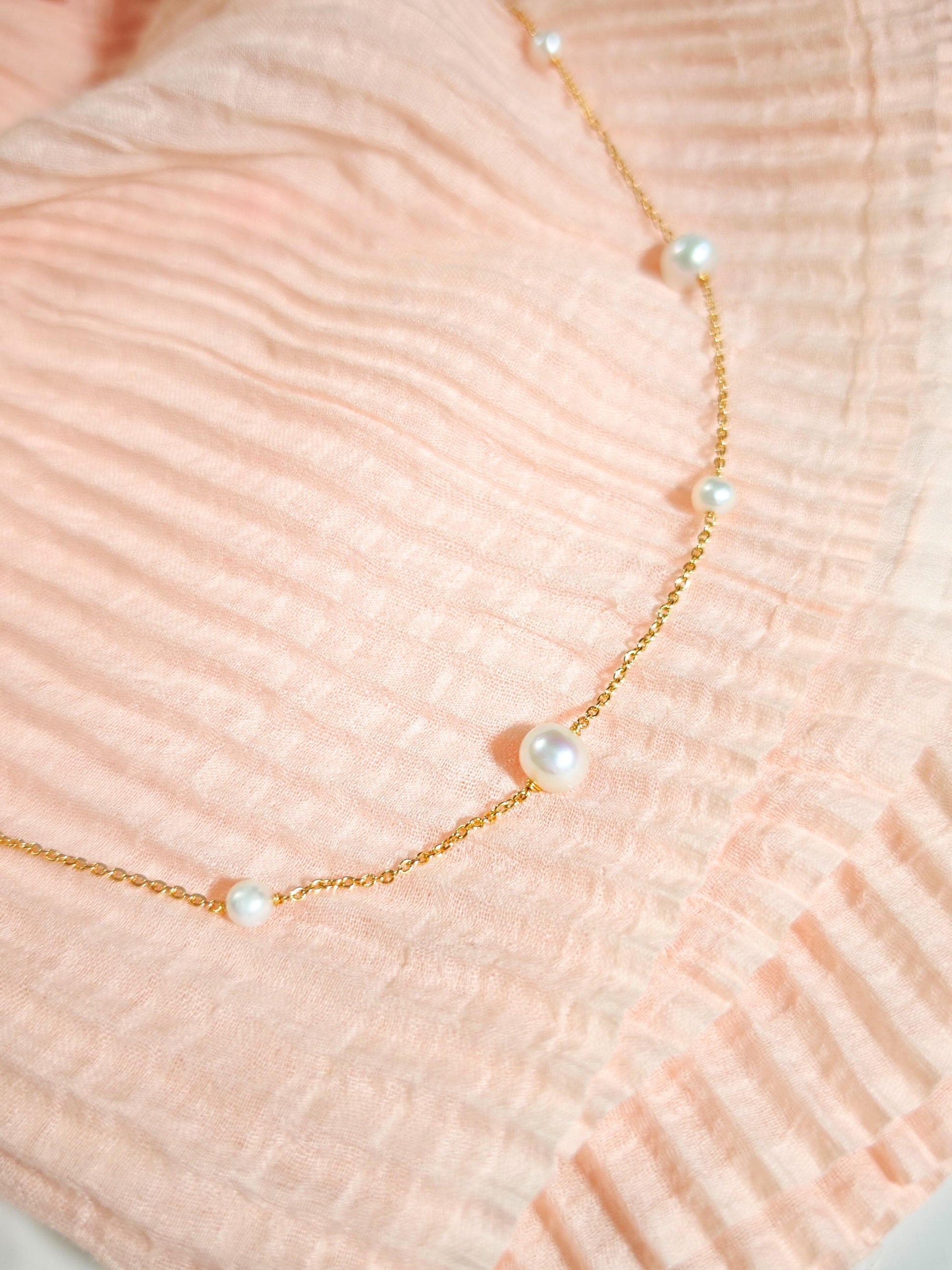Gold necklace with pearls on a textured peach fabric background