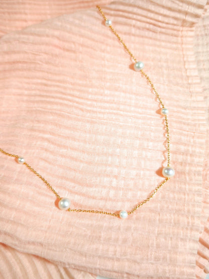 Gold necklace with pearls on a textured pink background