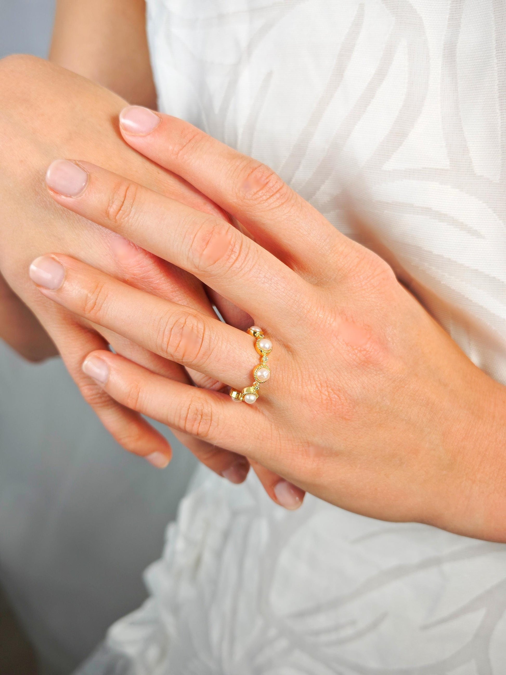 Close-up of a hand wearing a pearl ring with a blurred background
