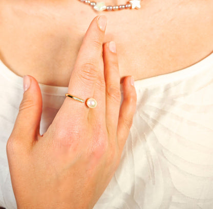 Close-up of a hand wearing a gold ring with a pearl on a white background