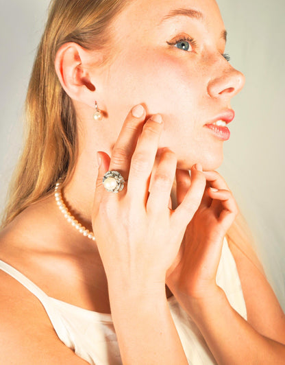 Woman wearing a pearl earring and ring, with a plain background