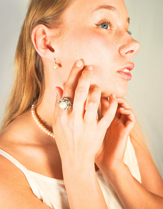 Woman wearing a pearl earring and ring, with a plain background