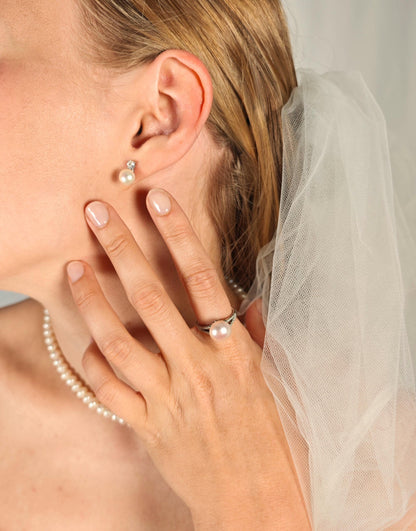 Close-up of a person wearing pearl earrings and a ring, with a blurred background.