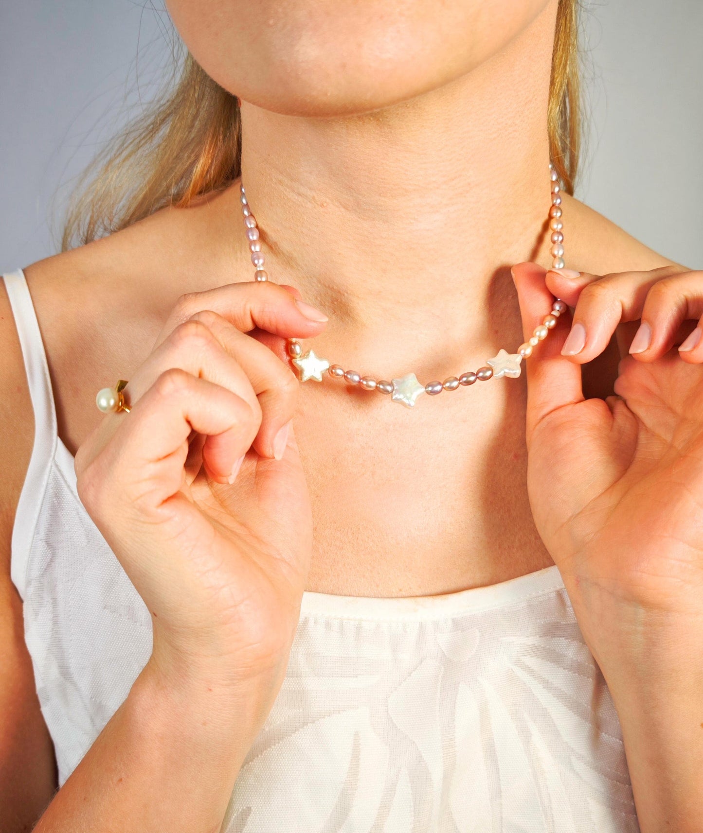 Person wearing a delicate necklace with star-shaped pendants against a neutral background