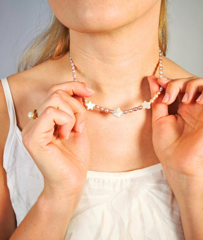 Person wearing a delicate necklace with star-shaped pendants against a neutral background