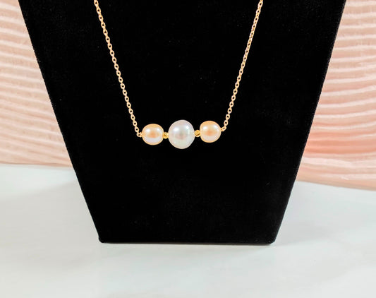 Pearl necklace on a black stand with a soft pink background