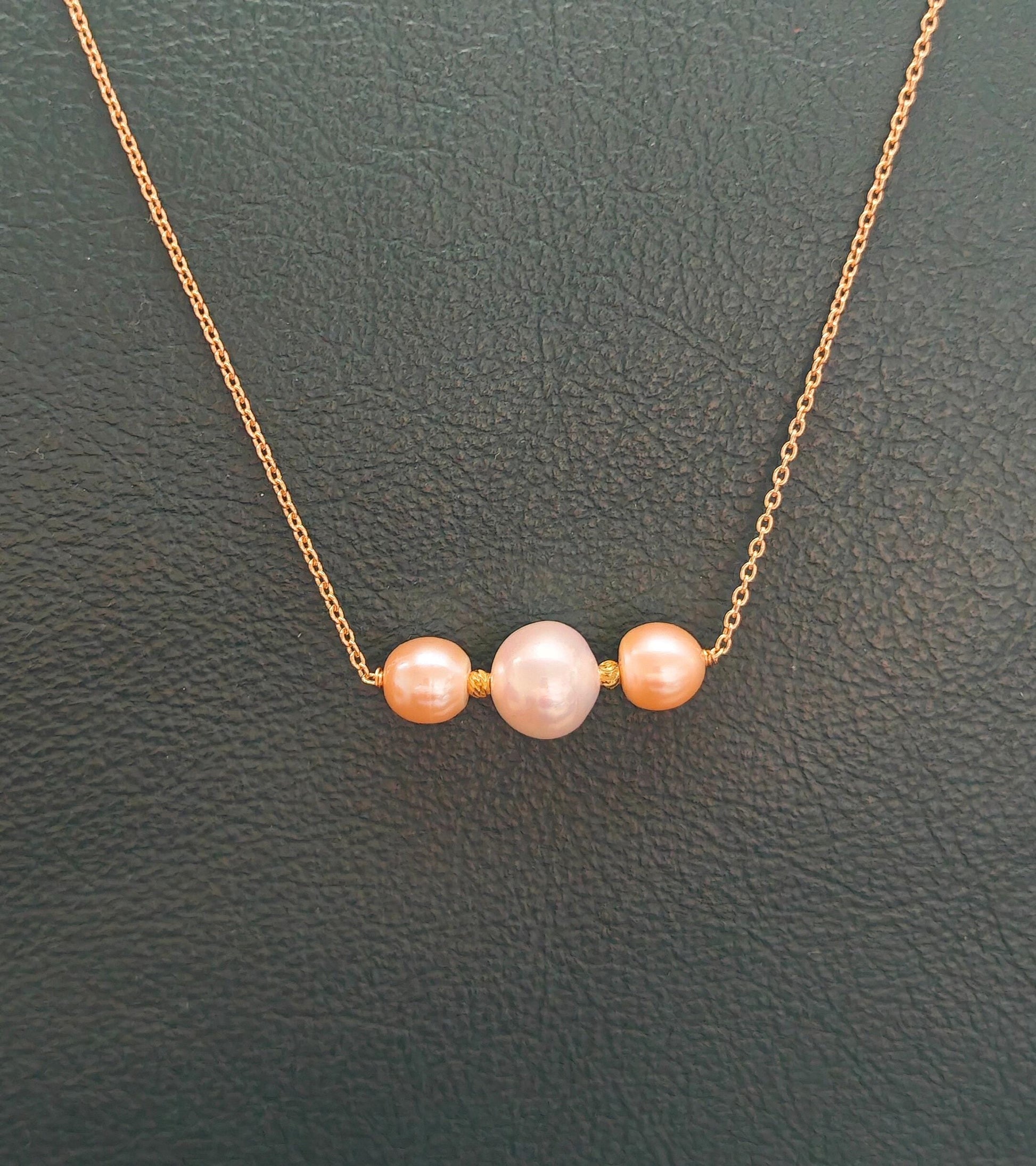 Necklace with three pink pearls on a gold chain against a dark green background