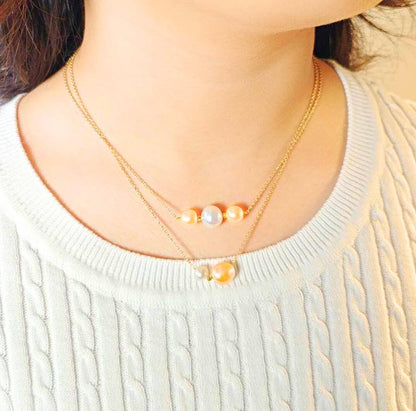 Necklace with pearl and orange bead on a light sweater