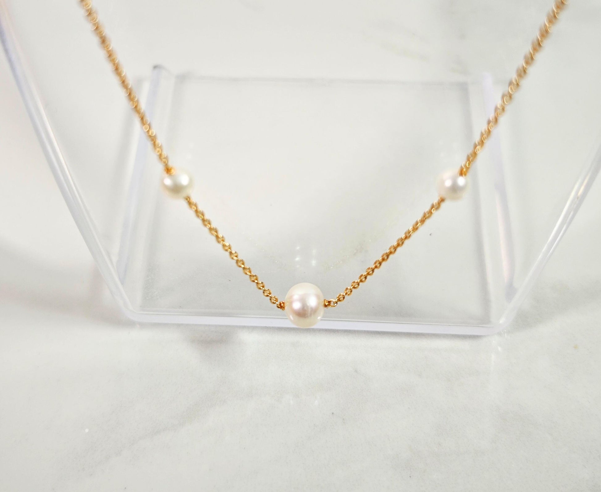 Gold necklace with pearls on a clear stand against a light background
