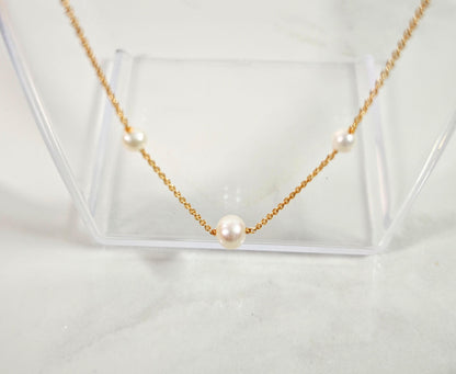 Gold necklace with pearls on a clear stand against a light background