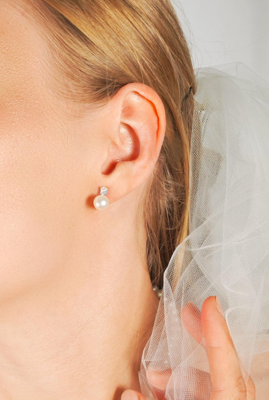 Close-up of a person wearing a pearl earring with a veil in the background