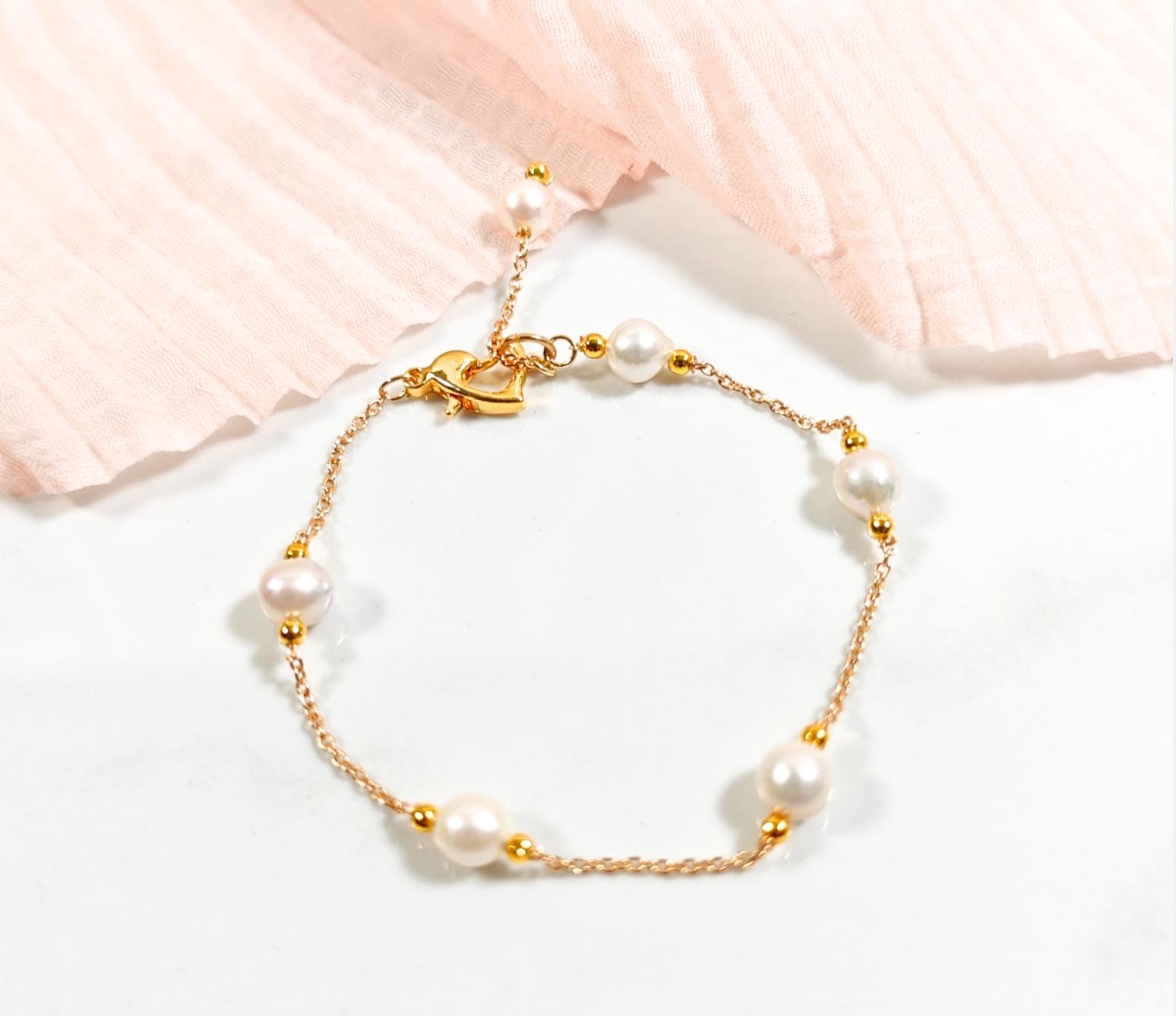Pearl bracelet with gold accents on a soft pink fabric background