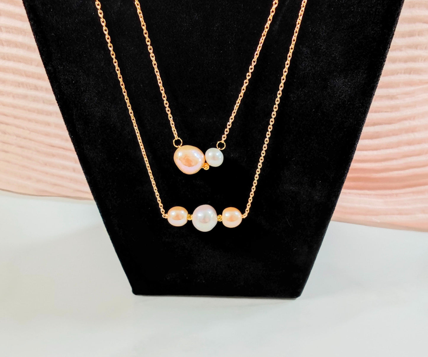 Gold necklace with pearl-like beads on a black stand with a light wooden background