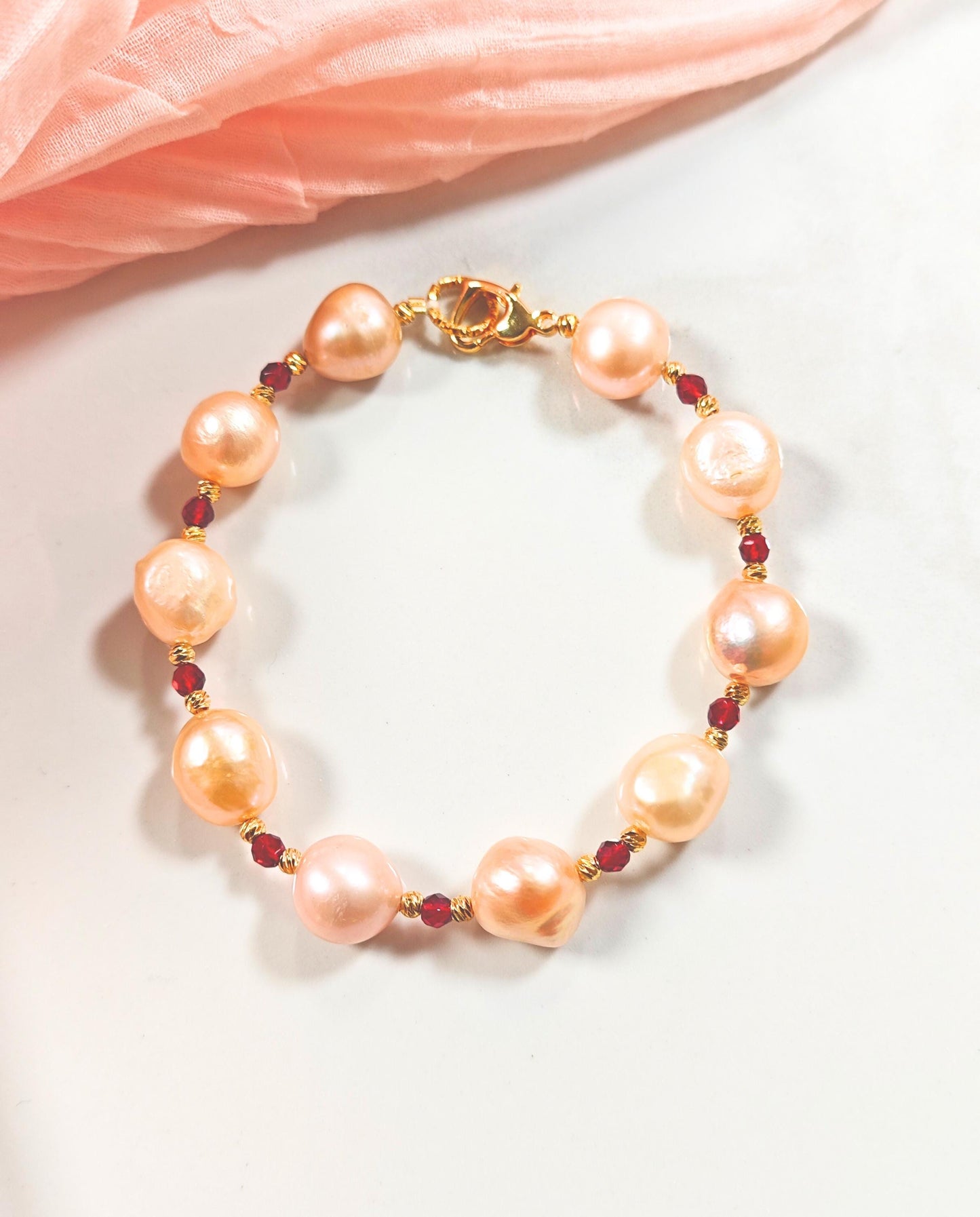 Pearl bracelet with gold accents and red beads on a light pink fabric background