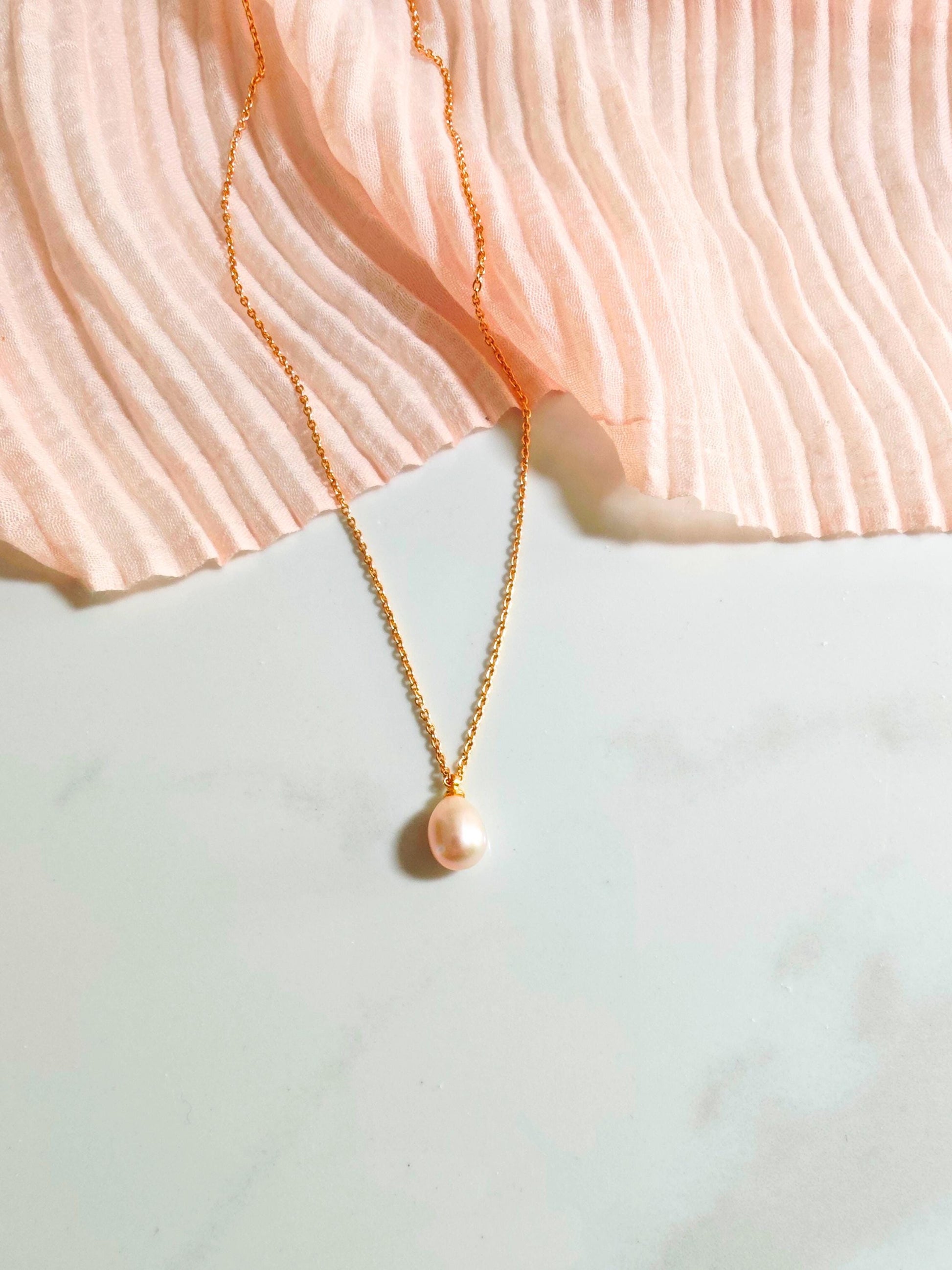 Gold necklace with a pearl pendant on a textured fabric background