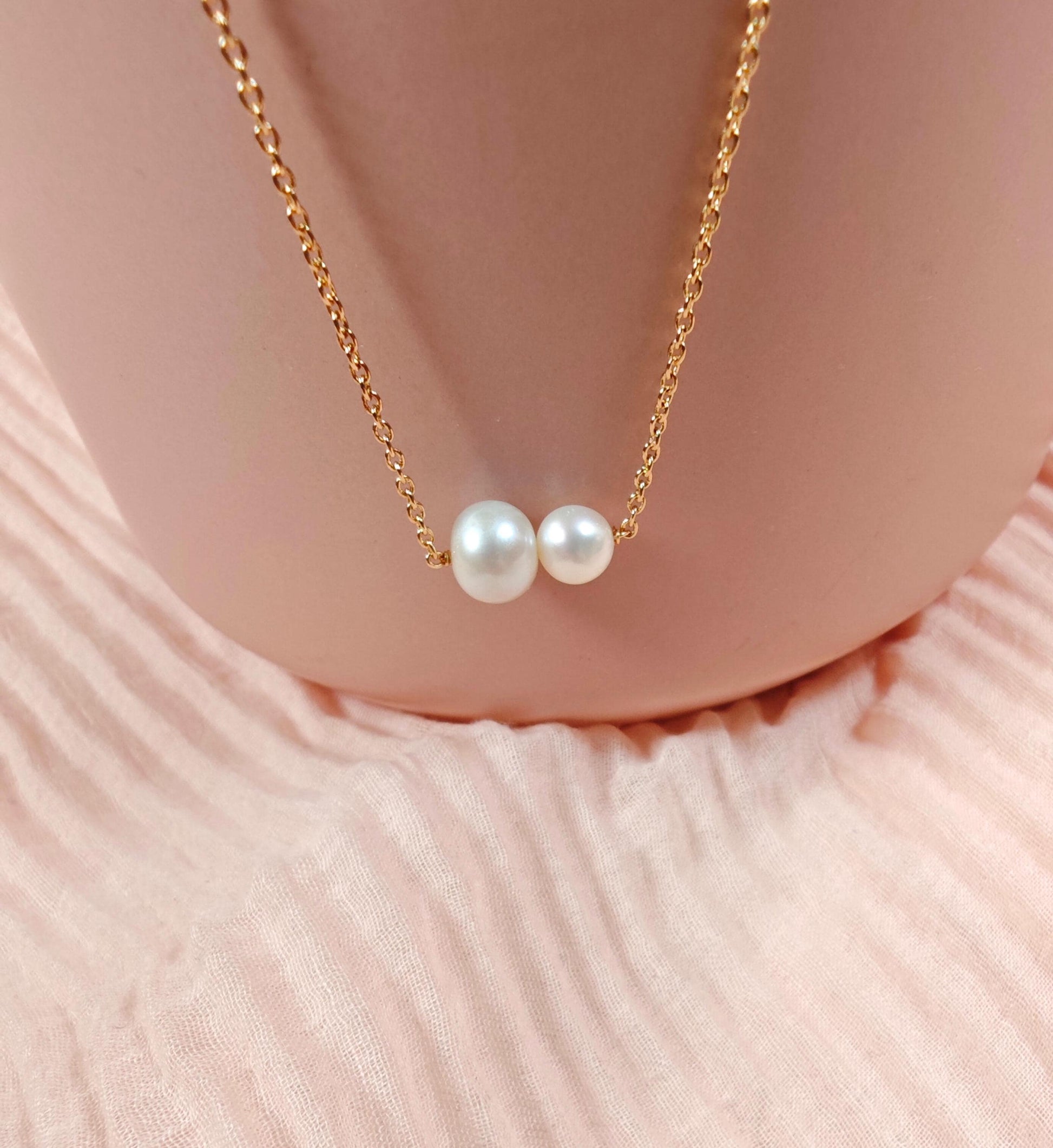 Pearl necklace with gold chain on a soft pink fabric background