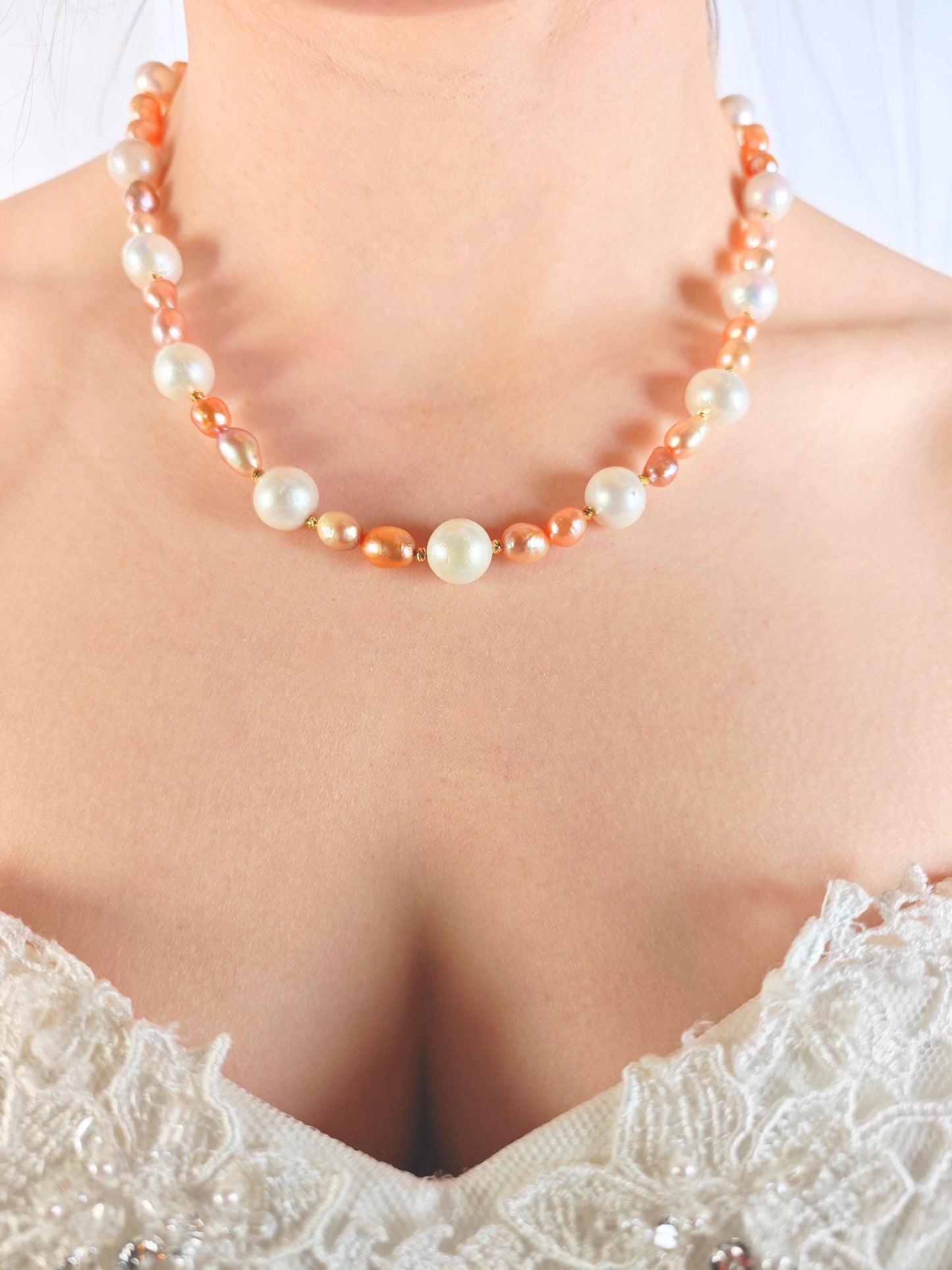 Pearl necklace with orange accents worn by a person in a white lace garment.