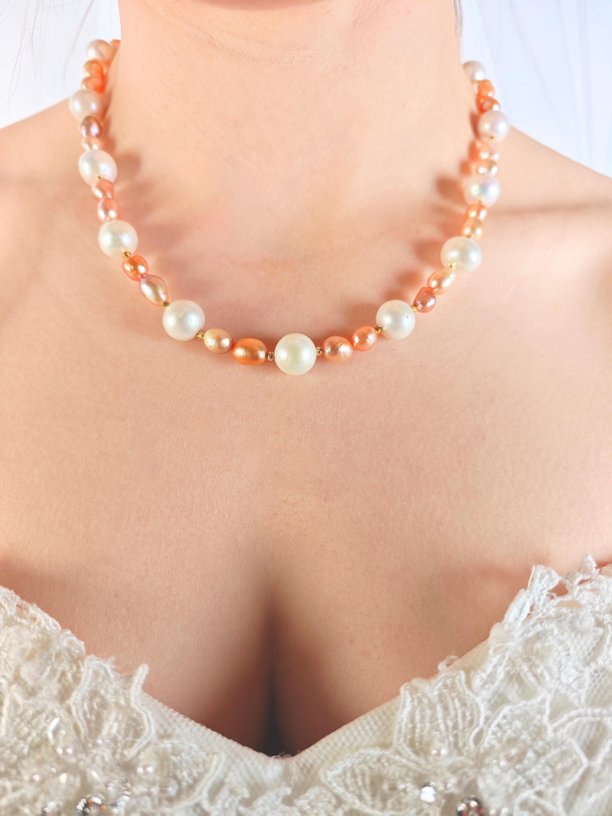 Pearl necklace with orange accents worn by a person in a white lace garment.