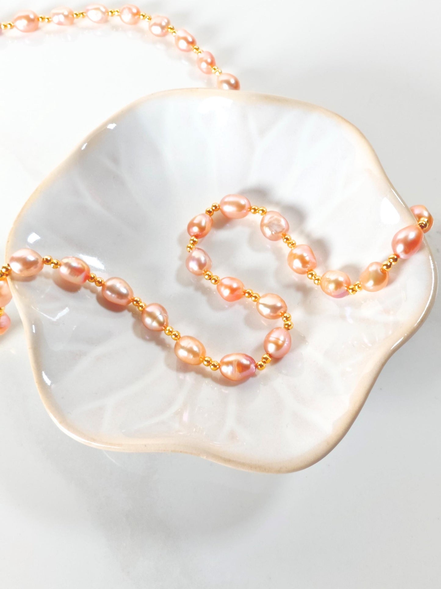 Pearl necklace on a white dish with a gold chain
