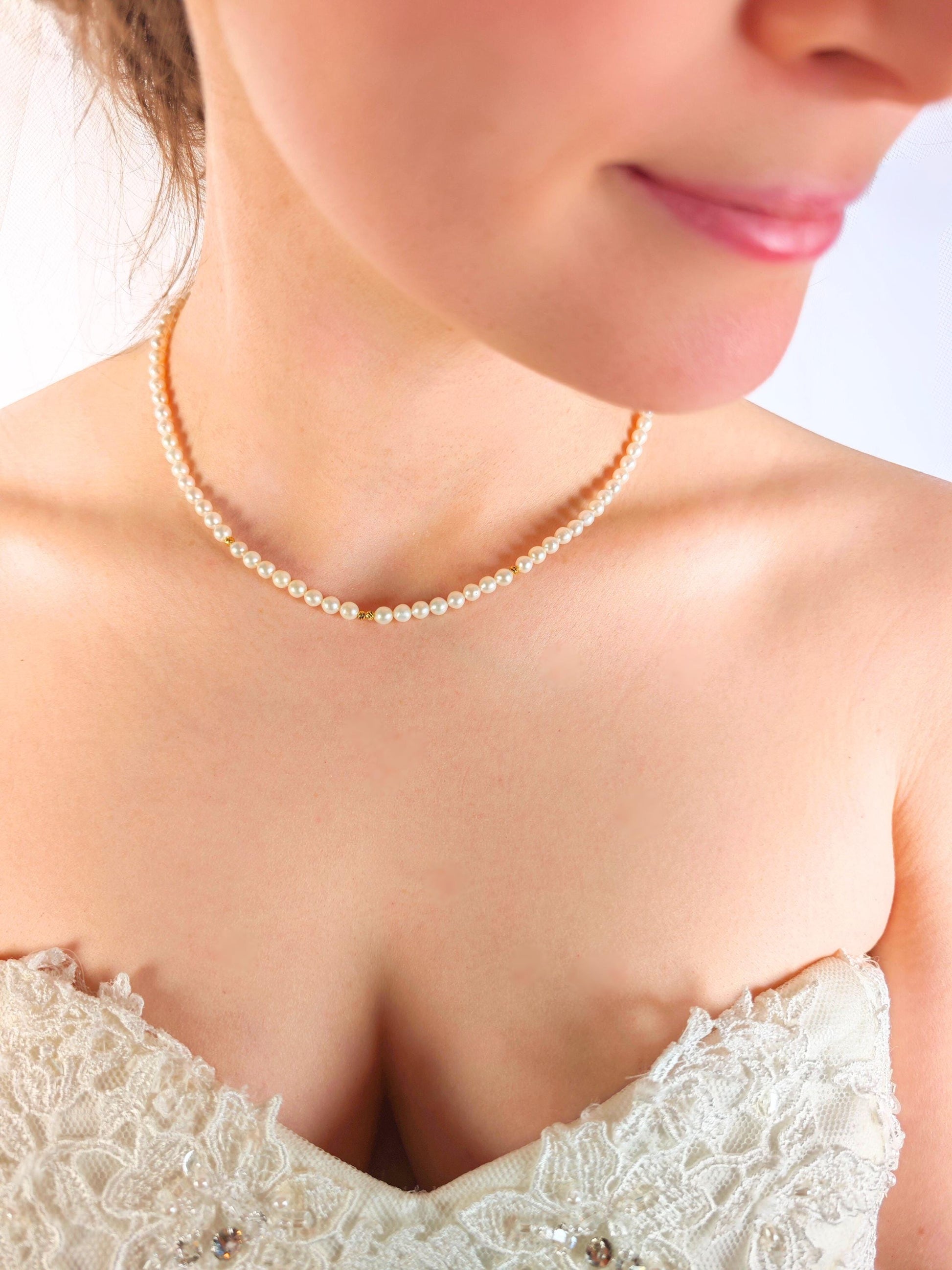 Pearl necklace worn by a person in a white lace garment against a light background