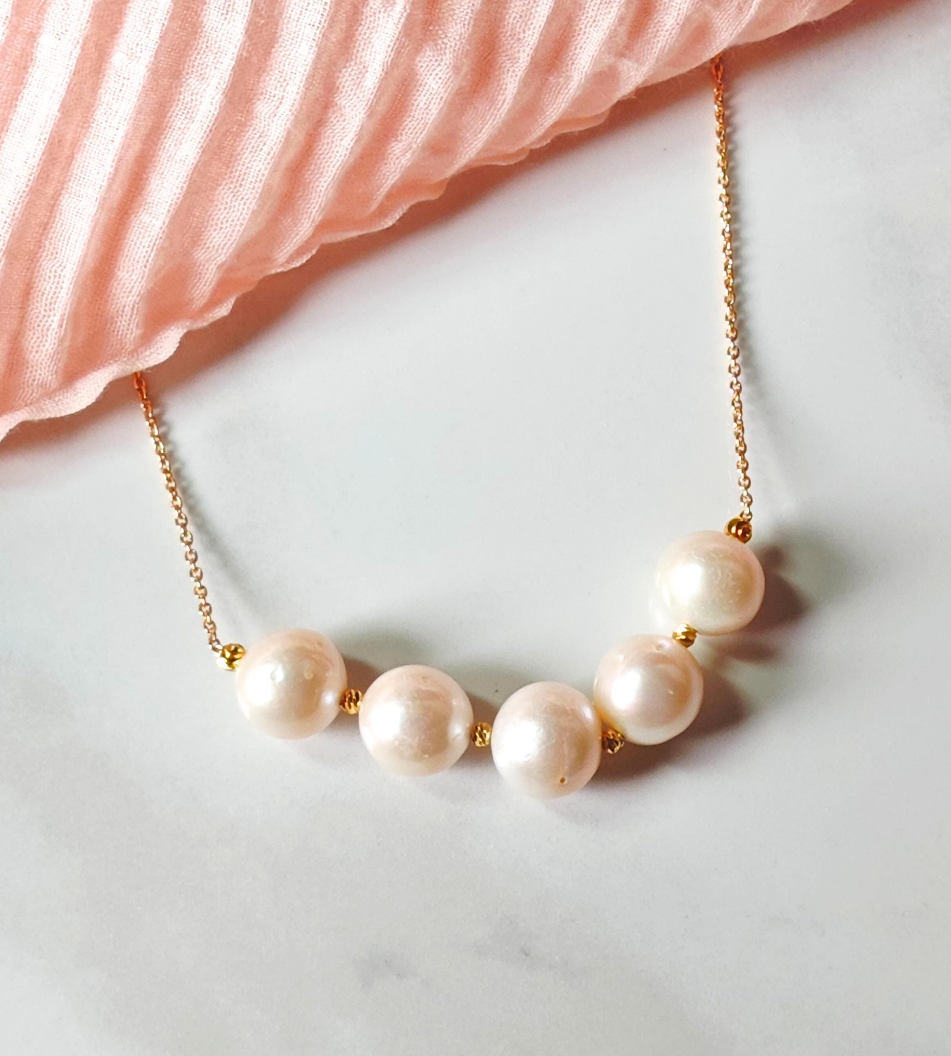 Pearl necklace with gold chain on a marble surface with pink fabric