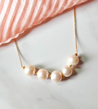 Pearl necklace with gold chain on a marble surface with pink fabric