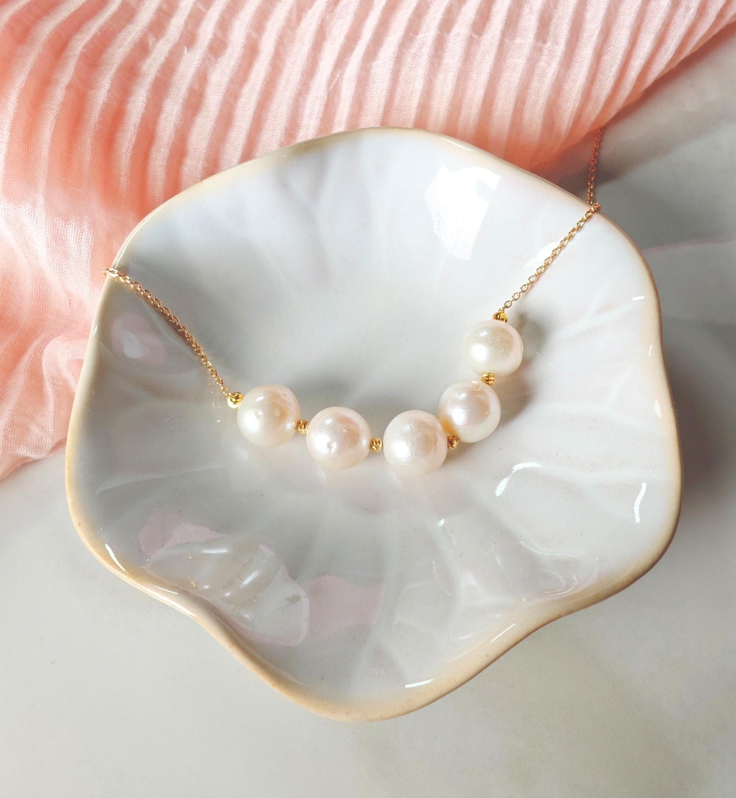 Pearl necklace on a white dish with a pink fabric background
