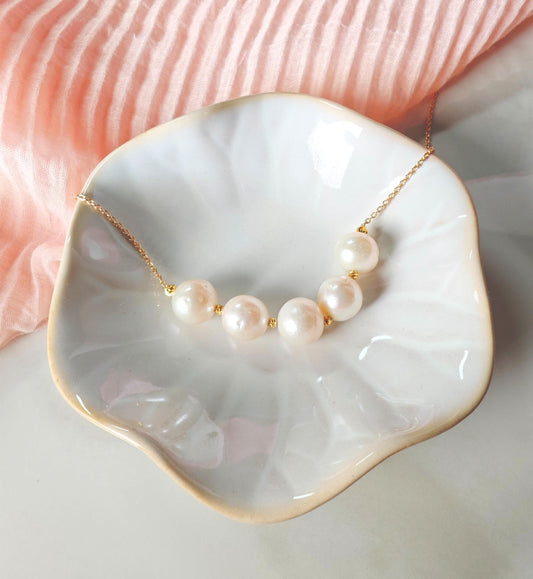 Pearl necklace on a white dish with a pink fabric background