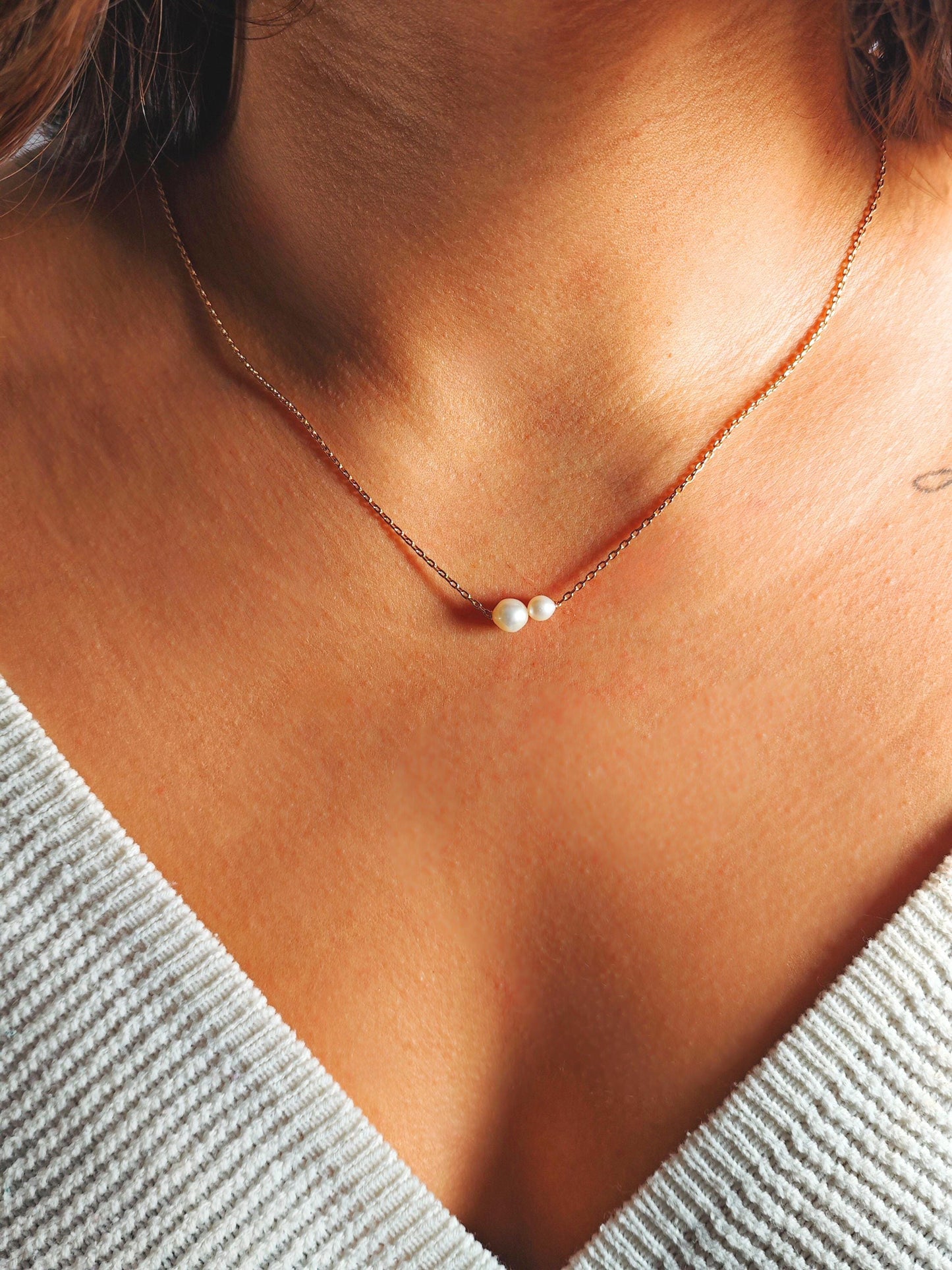 Necklace with a pearl pendant on a person wearing a light gray top.