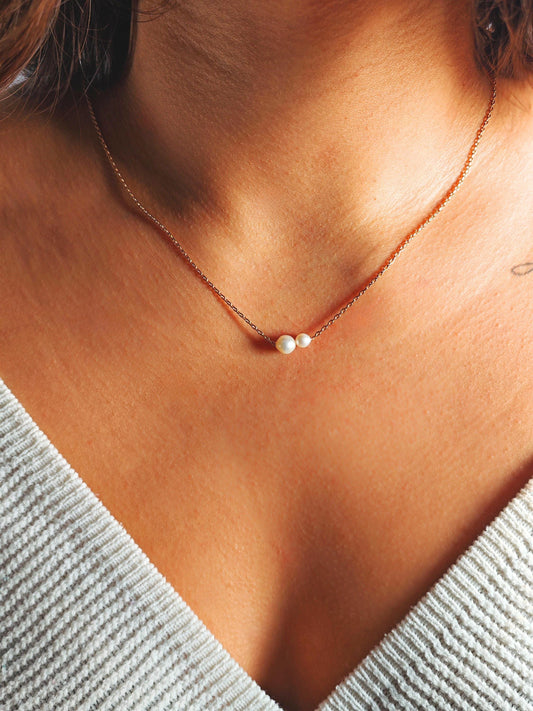 Necklace with a pearl pendant on a person wearing a light gray top.