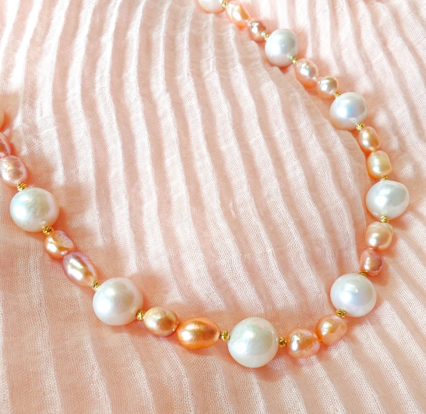Pearl necklace with pink and gold accents on a soft pink fabric background
