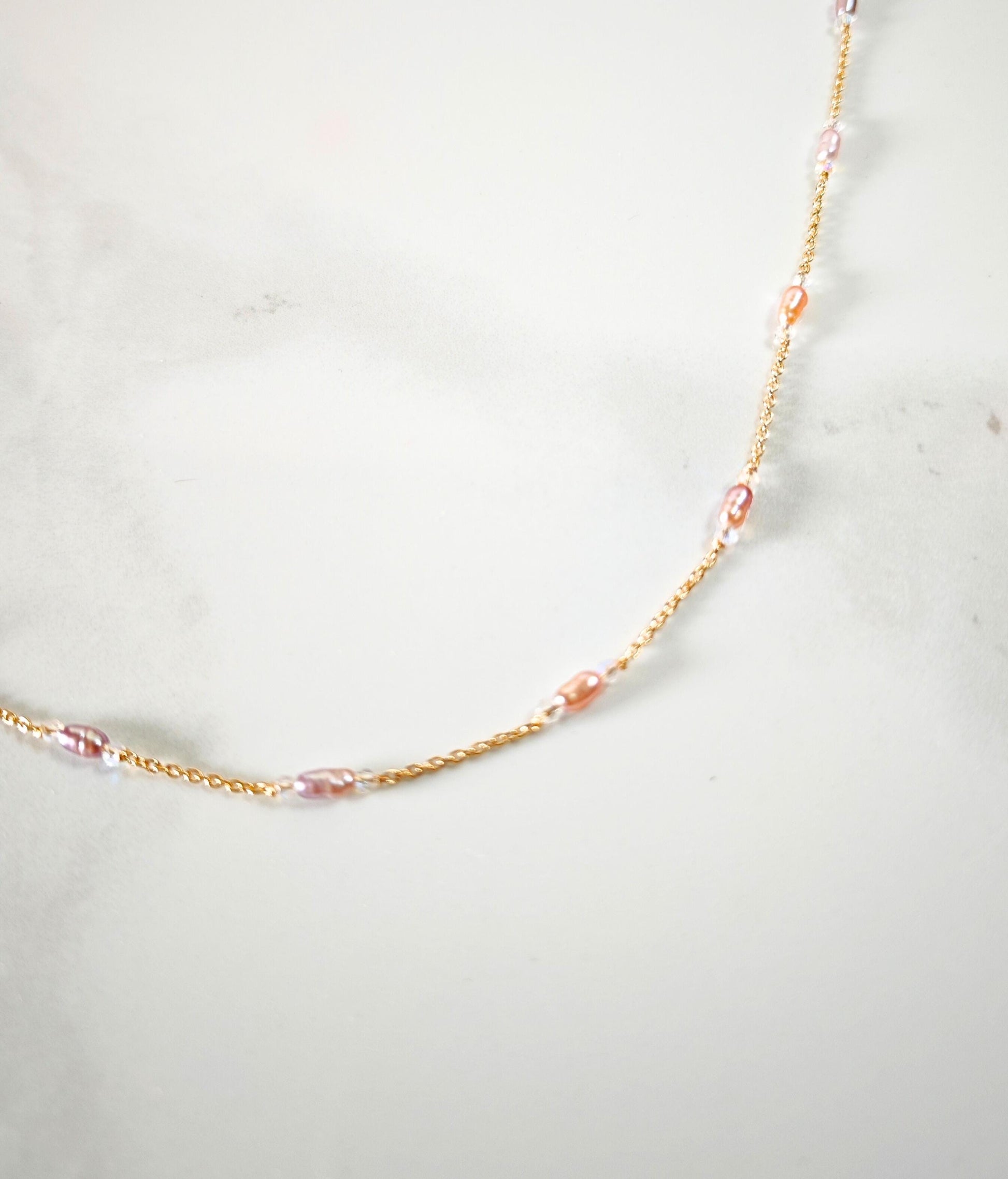 Necklace with pink beads on a gold chain against a light gray background