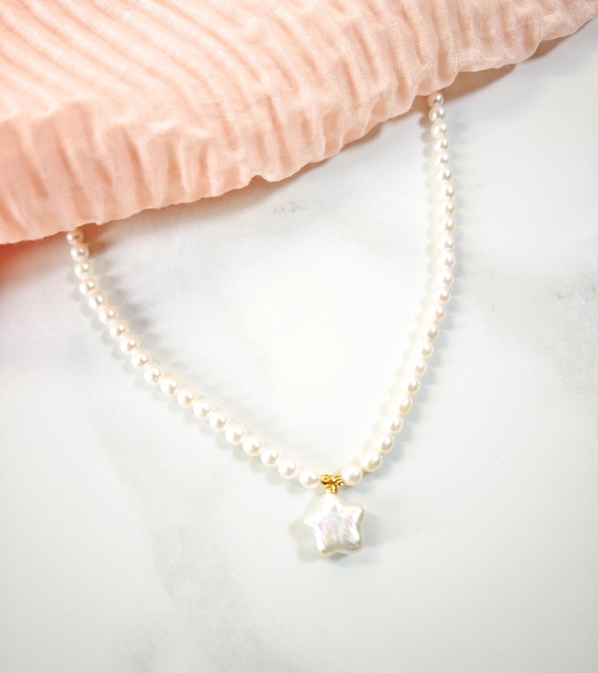 Pearl necklace with a star-shaped pendant on a light pink fabric background
