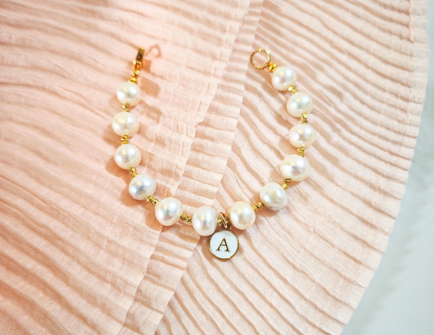 Pearl necklace with a gold clasp and letter 'A' charm on a textured pink surface