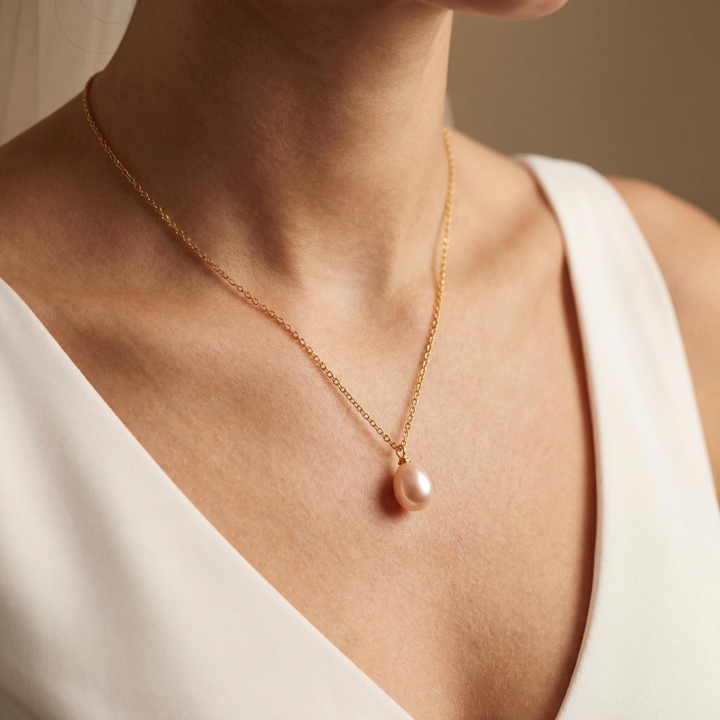 Gold necklace with a pendant worn by a person in a white top against a neutral background