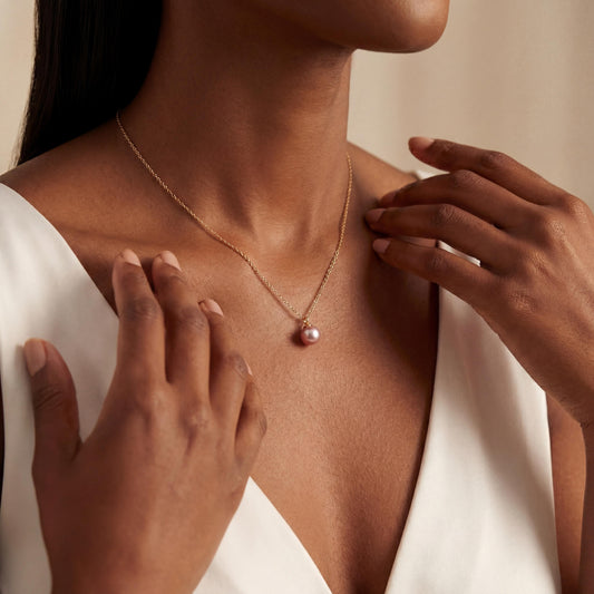 Woman wearing a gold necklace with a pink pendant, hands adjusting it.