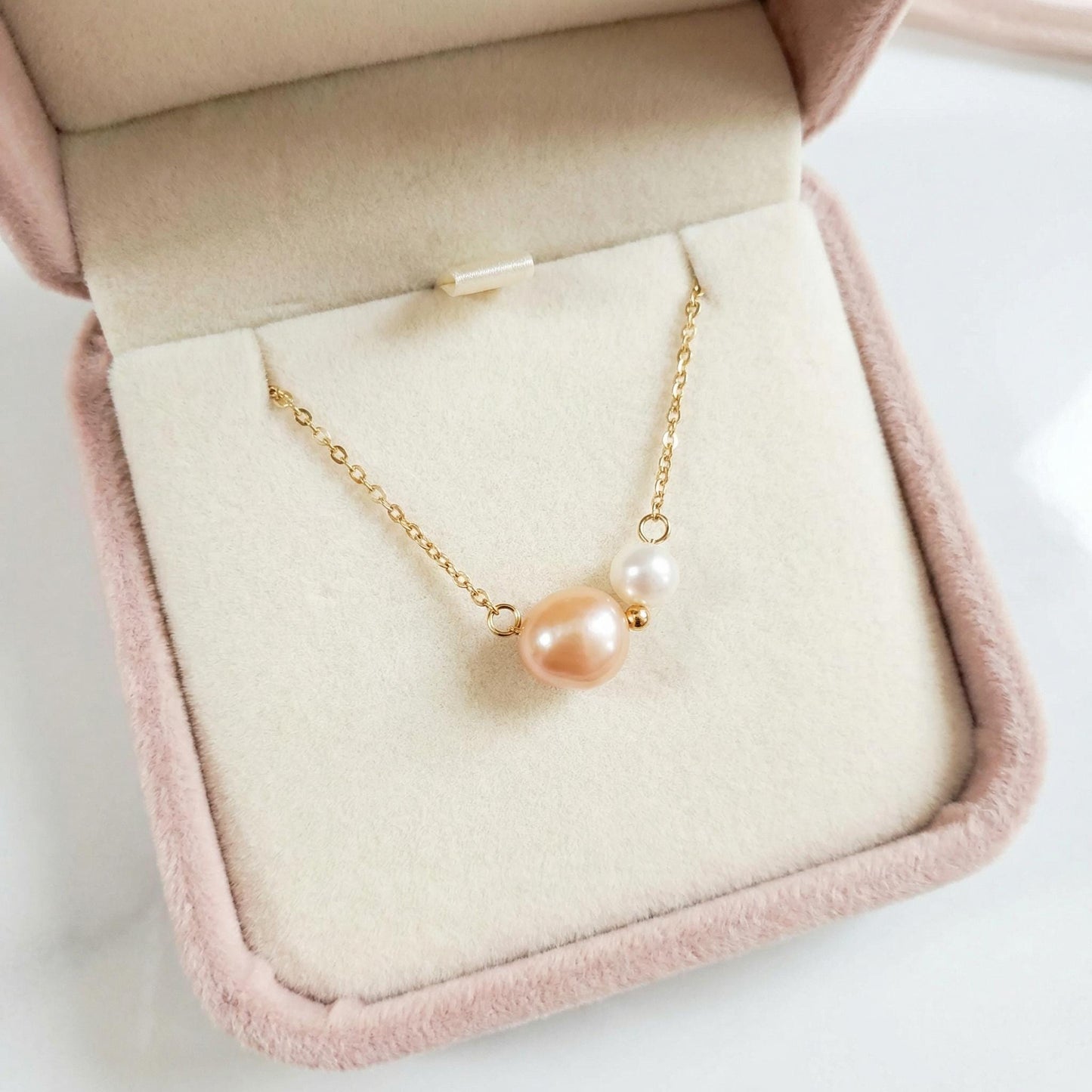 Pearl necklace on a pink jewelry box with a white background