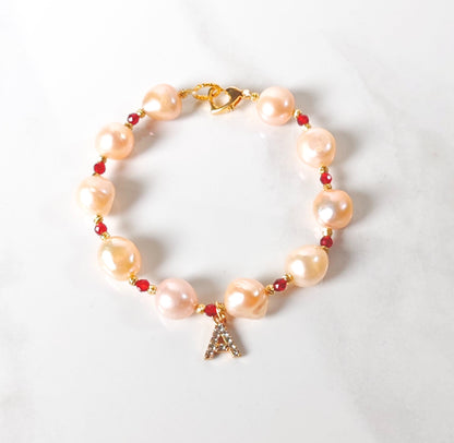 Pearl bracelet with red beads and a gold charm on a white background
