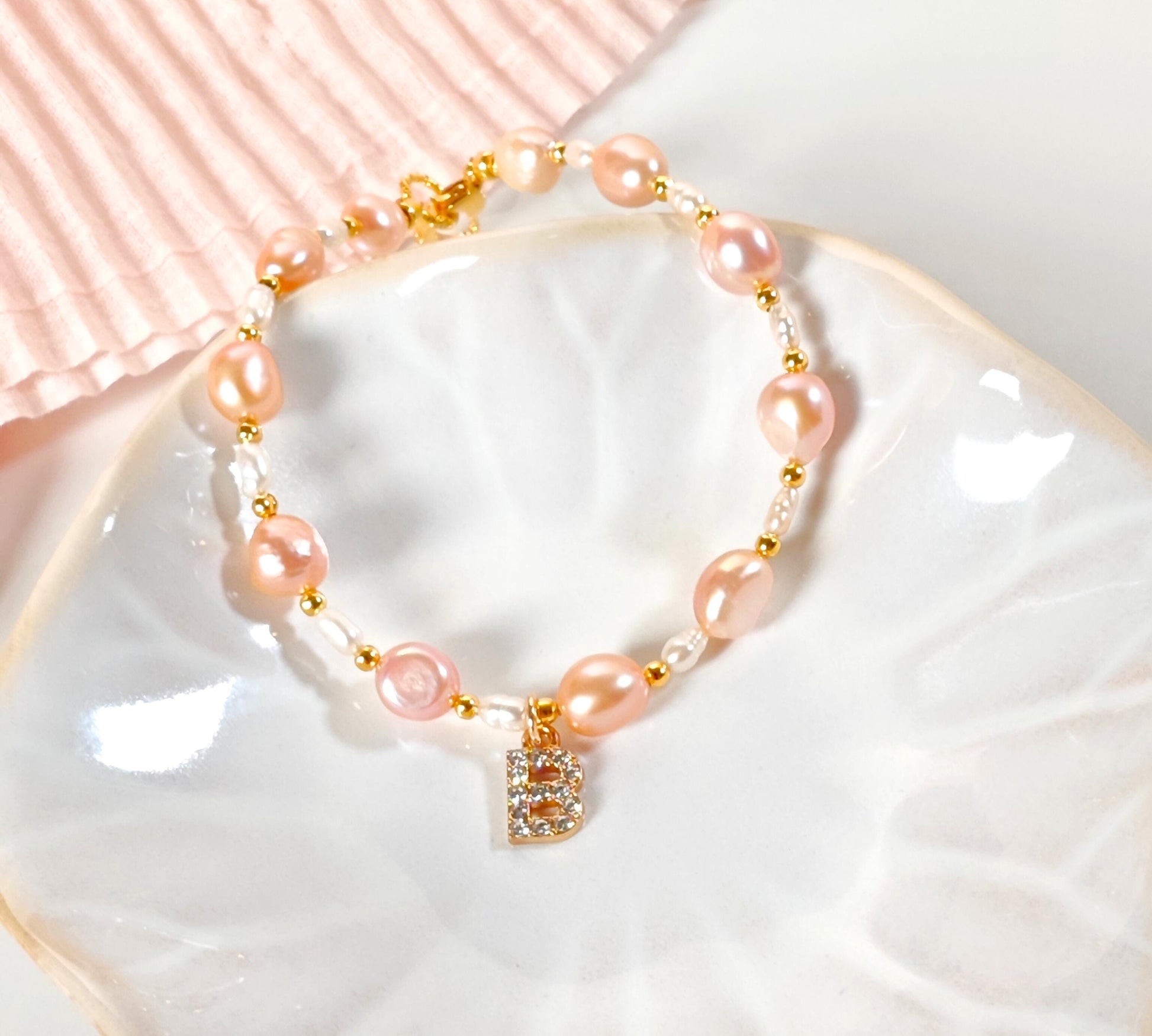 Pink pearl bracelet with a gold clasp on a white dish