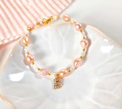 Pink pearl bracelet with a gold clasp on a white dish