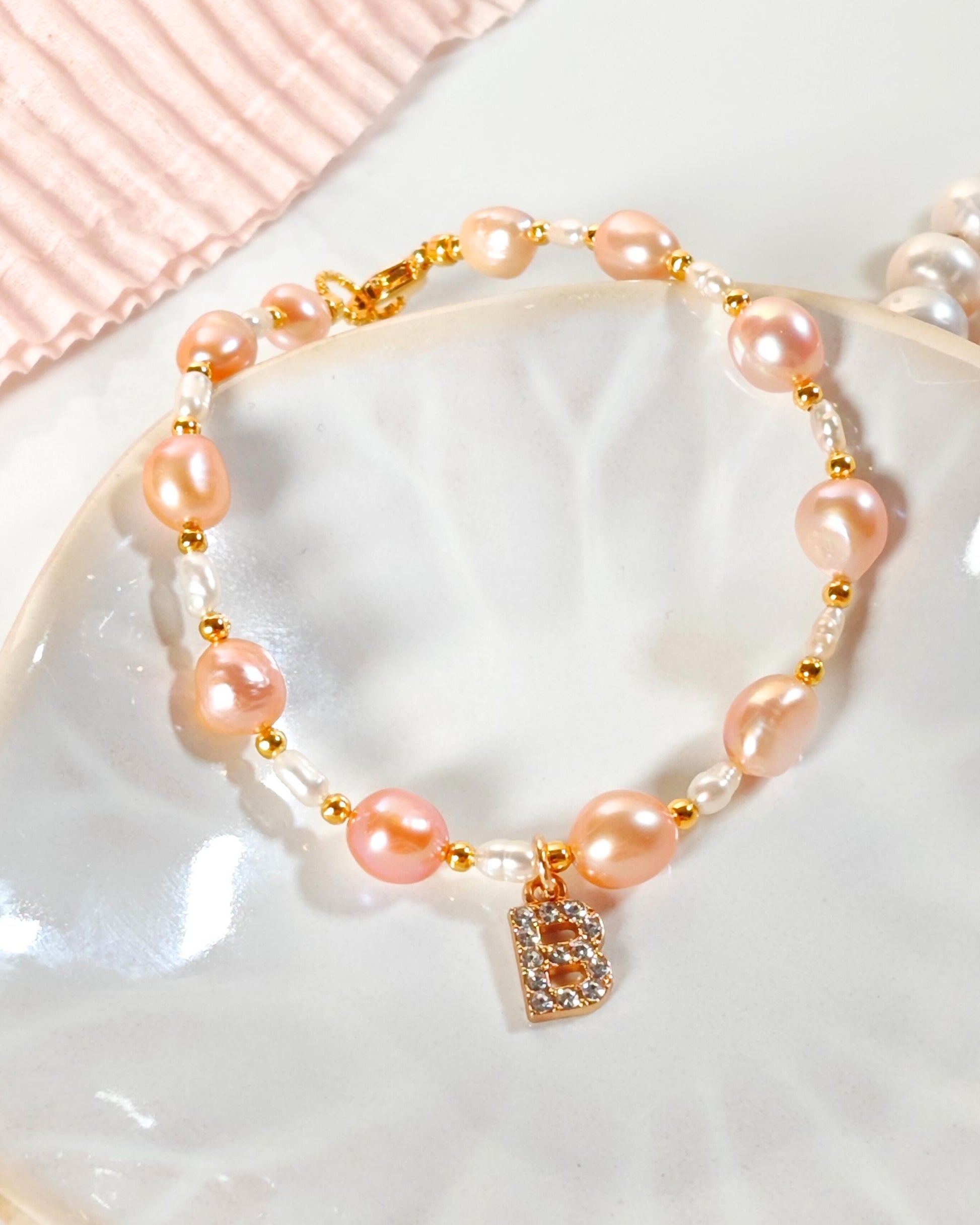 Pearl bracelet with pink beads and a gold clasp on a white dish.